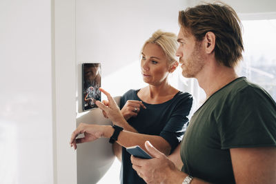 Mature couple adjusting digital tablet mounted on wall at home