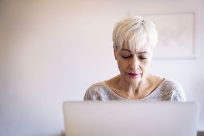 Senior woman using laptop computer against wall at home