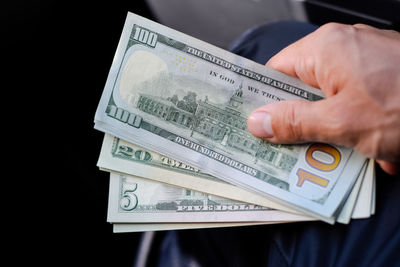 Midsection of man holding paper currency against black background