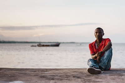 Portrait of young man sitting against sea against sky