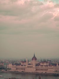 Buildings at waterfront against cloudy sky