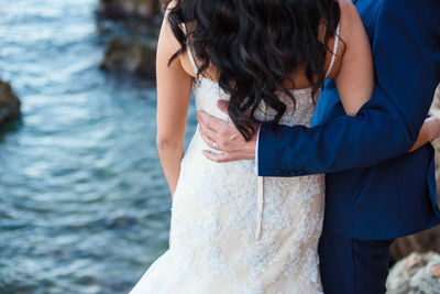 Midsection of newlywed couple standing by sea