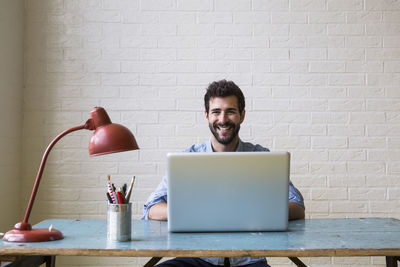 Portrait of happy young man sitting at desk working with laptop
