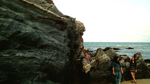 People relaxing on rock by sea against sky