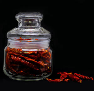 Close-up of red chili pepper in jar against black background