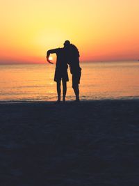 Silhouette friends standing on beach during sunset