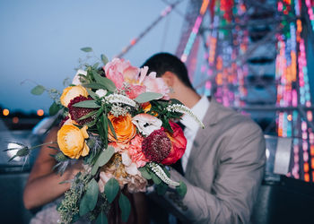 Couple covering face with flower bouquet during wedding ceremony