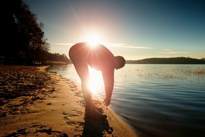 Rear view of silhouette man standing at beach against sky during sunset