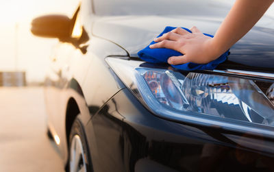 Cropped hand of person cleaning car on street during sunset