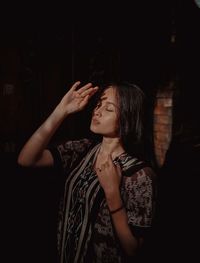 Young woman looking away while standing against black background