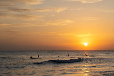 Silhouette people swimming in sea against sky during sunset