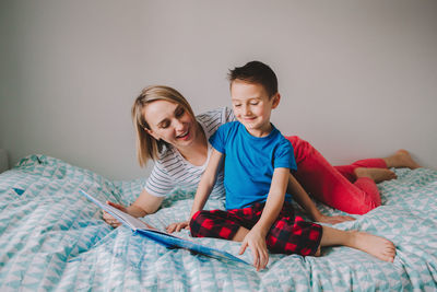 Cute boy reading book while lying on bed with mother at home