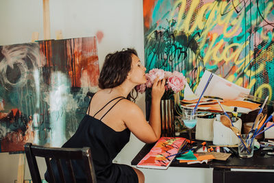 Woman artist smelling flowers while sitting at her workshop