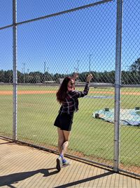 Young woman looking away while standing by chainlink fence