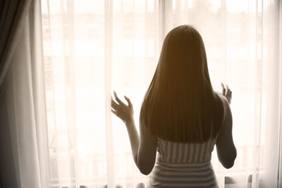 Rear view of woman looking through window at home