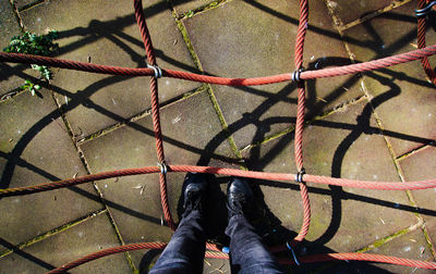 Low section of person standing amidst ropes in playground