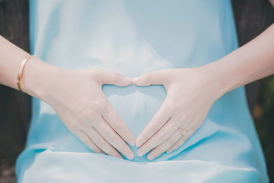 Midsection of woman making heart shape on white finger