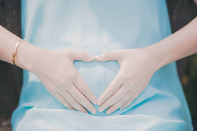 Midsection of pregnant woman making heart shape on abdomen