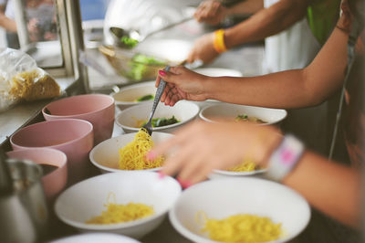 Cropped hand putting noodles in bowl at market stall