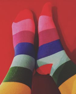 Low section of person wearing multi colored socks against red background