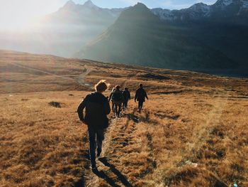 Rear view of friends walking on grassy field against mountains