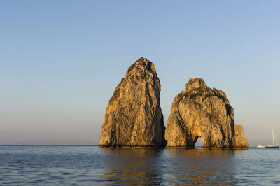 Rock formation in sea against clear sky