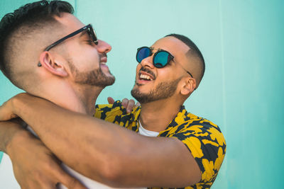 Gay men embracing while wearing sunglasses against wall