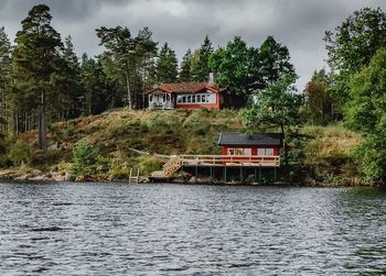 Scenic view of river by building and trees against sky