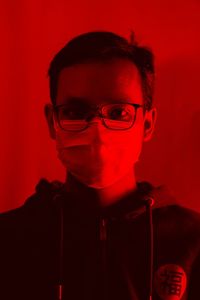 Portrait of man wearing flu mask standing against against red background
