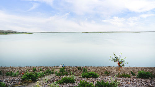 Scenic view of men sitting at the lakeside against sky