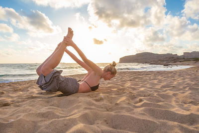 Young woman lying on sand at beach against sky