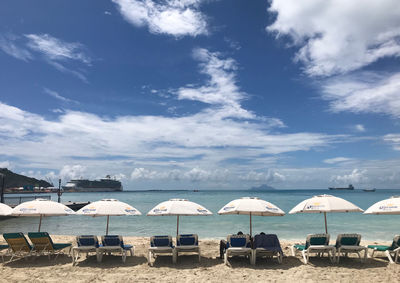 Lounge chairs and parasols on beach against sky