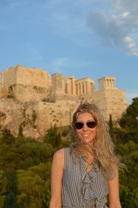 Portrait of young woman wearing sunglasses standing against historic building