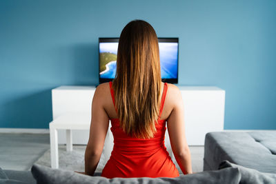 Rear view of woman watching tv while sitting on sofa at home