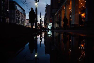 People standing by puddle on footpath at night