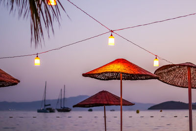 Umbrellas by sea against sky during sunset