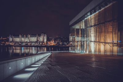 Illuminated buildings by river against sky at night