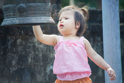 Cute baby girl looking at bell while standing outdoors