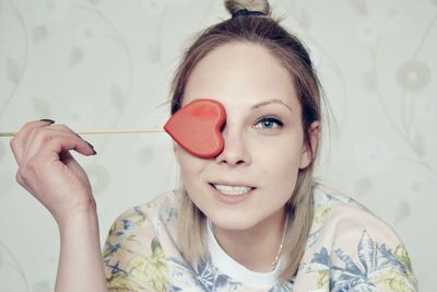Portrait of young woman covering eye with heart shape candy