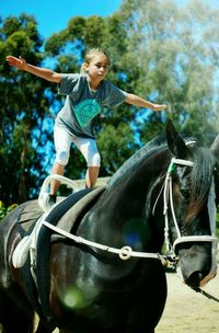 Girl balancing on horse during sunny day