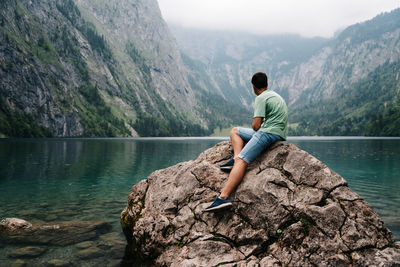 Full length of man sitting on rock at lakeshore