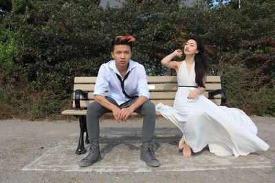 Portrait of young couple sitting on bench in park