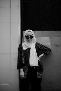 Portrait of young woman wearing sunglasses standing against wall