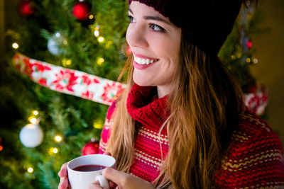 Young woman drinking coffee cup on christmas tree
