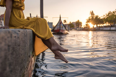 Side view of cropped unrecognizable female tourist legs sitting while enjoying rippled river in aveiro portugal in back lit with sunset