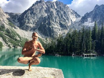 Shirtless man practicing yoga on rock by colchuck lake against mountain