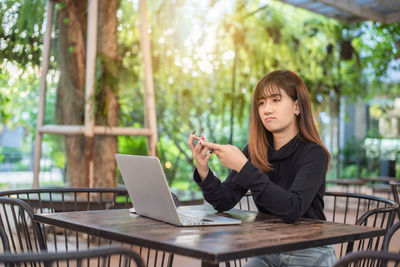 Young woman using phone while sitting on table