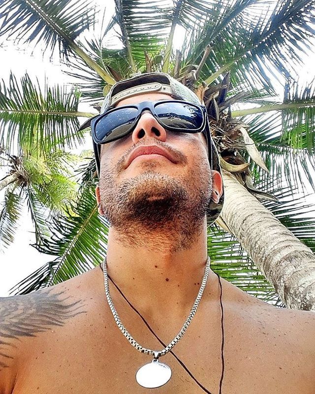 palm tree, tree, portrait, looking at camera, low angle view, front view, sunglasses, young adult, sunlight, outdoors, sky, day, leisure activity, art, lifestyles, person, beach, smiling