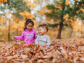 Smiling kids sitting on autumn leaves outdoors