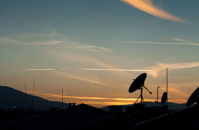 Silhouette of satellite dishes against sky during sunset